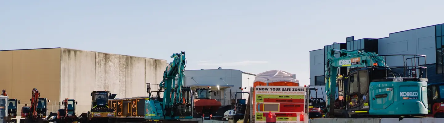 Construction site with various equipment, a water truck spraying dust control, and water-filled safety barriers in place.
