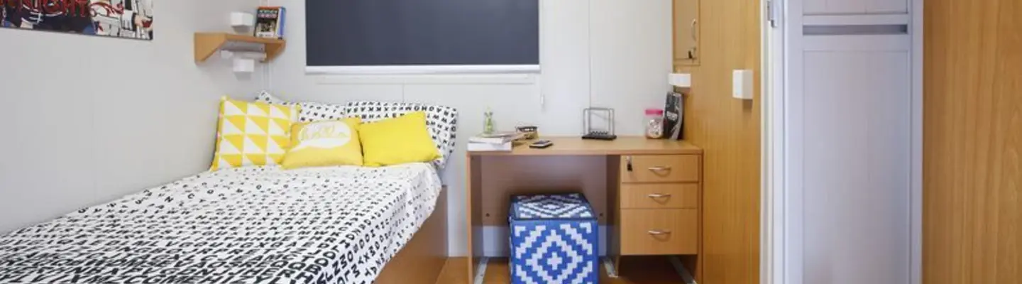Compact modular bedroom with single bed, desk, storage, and air conditioning.