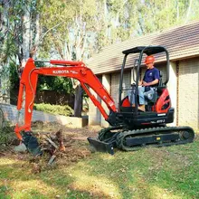Worker operating a mini excavator on a construction site, showcasing compact equipment used in barrier installation projects.